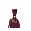 Burgundy faux leather knot handbag with gathered drawstring closure. Sculpted evening clutch or wristlet bag.